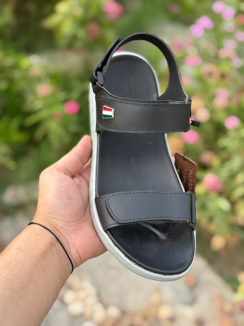 Black sandal held in a hand with a blurred floral background